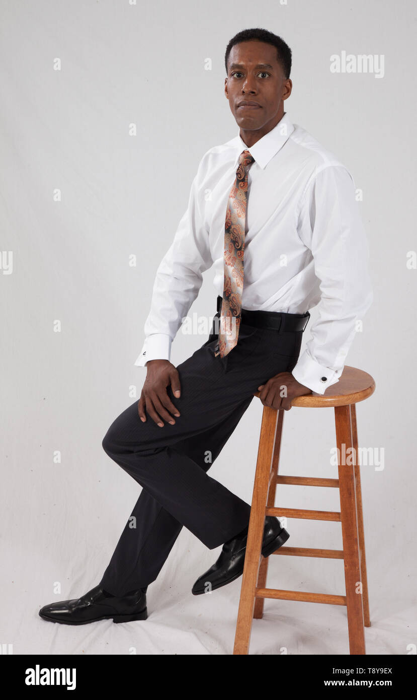 Black business man in white shirt and tie sitting on a wooden stool Stock Photo
