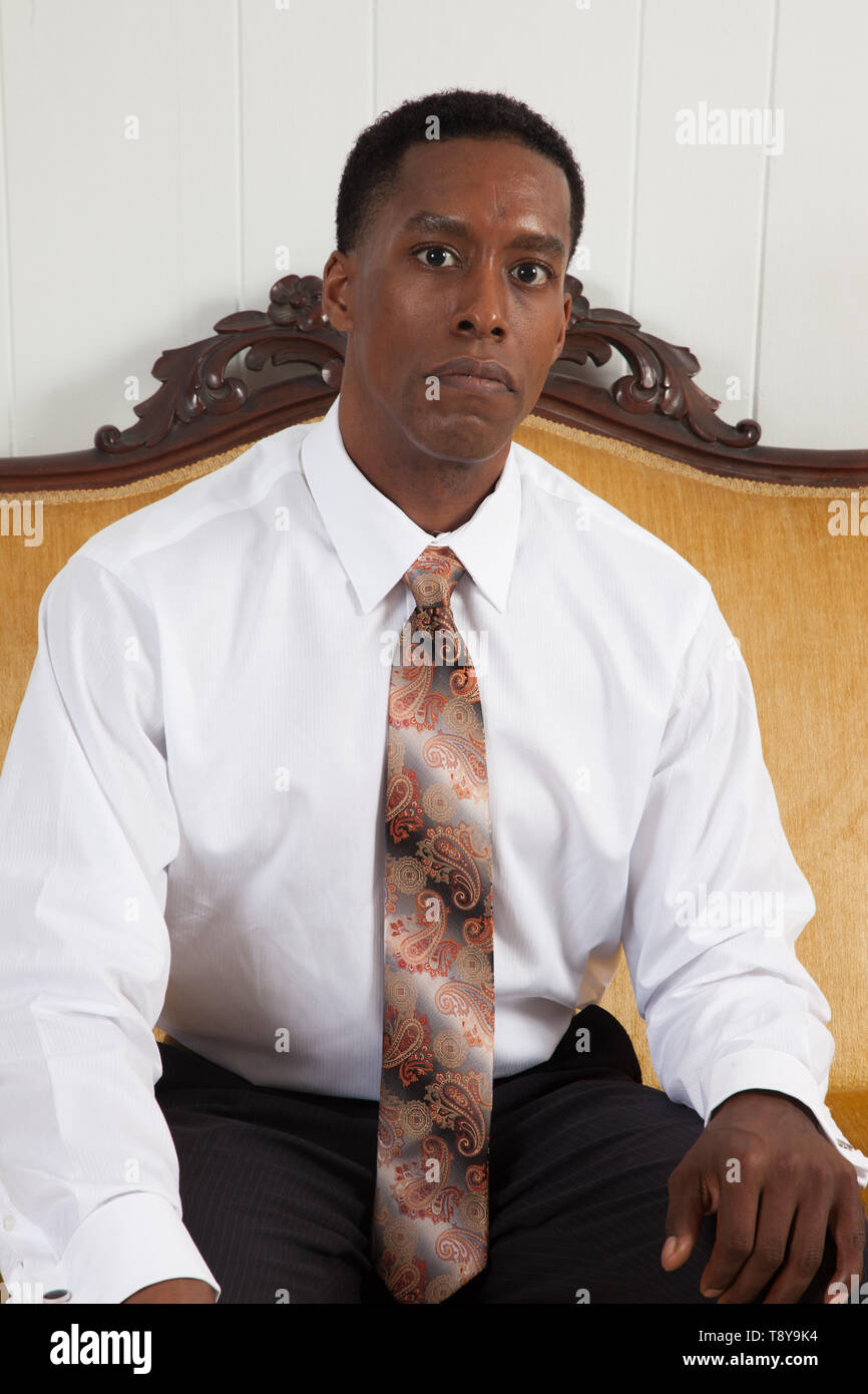 Handsome Black Man In A White Shirt And Tie Sitting On A Gold Couch Stock  Photo - Alamy