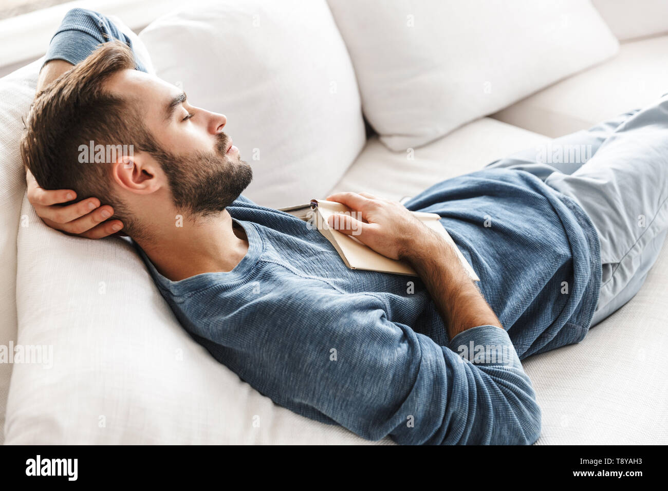 Attractive young man relaxing on a couch at home, sleeping Stock Photo