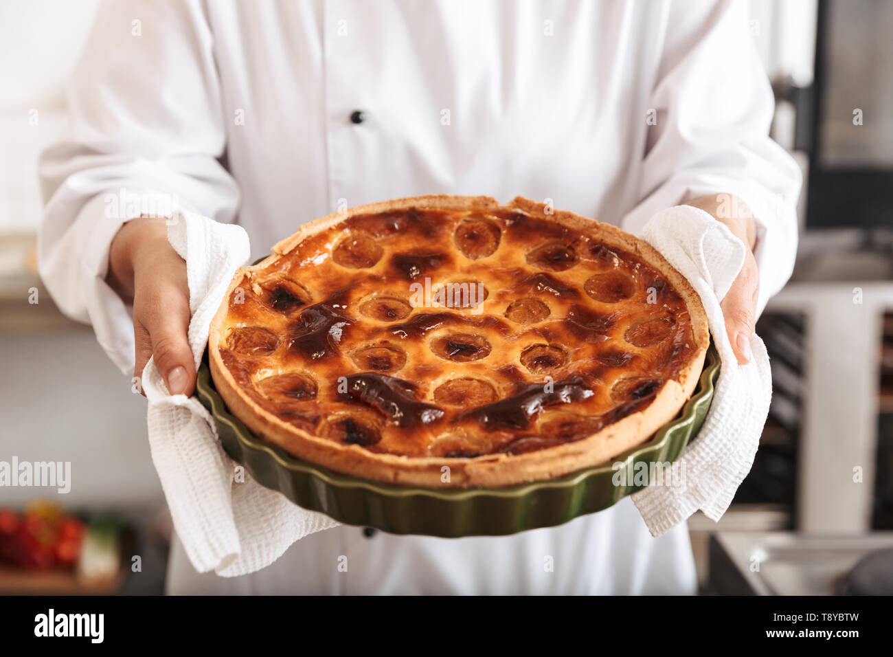 Image of young woman chef wearing white uniform holding apple pie while ...