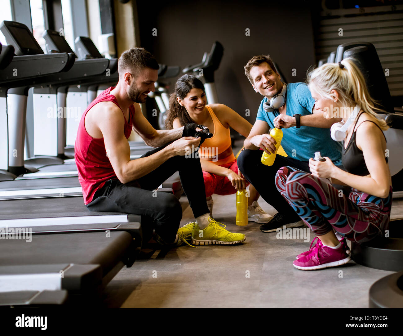 Group of young people in sportswear talking and laughing together while  sitting on the floor of a gym after a workout Stock Photo - Alamy