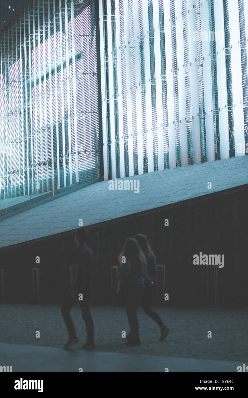 Group of people walking in a center of city at night. Backlit construction behind them Stock Photo