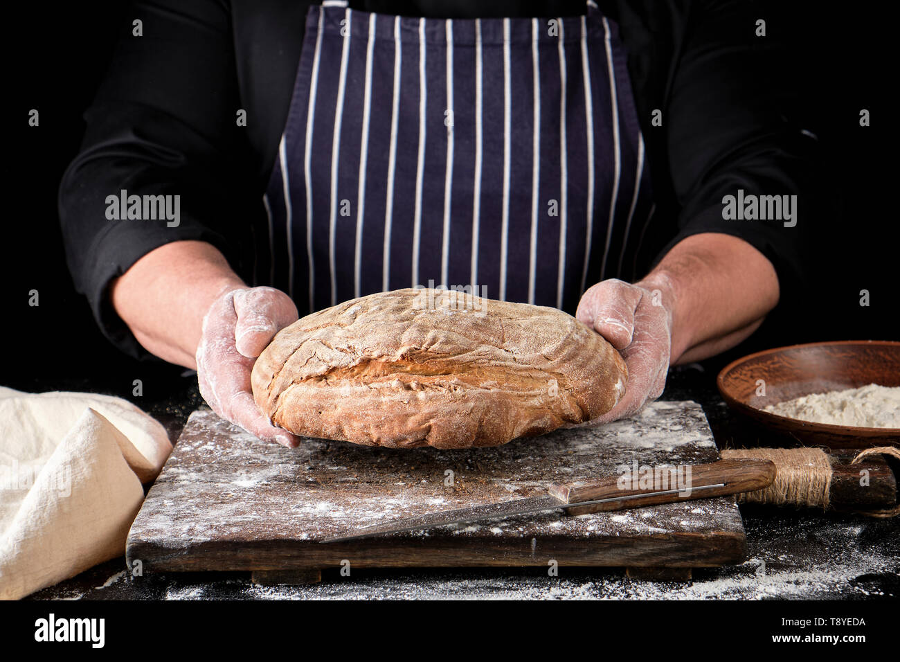 male hands are holding brown baked rye bread over wooden board with ...