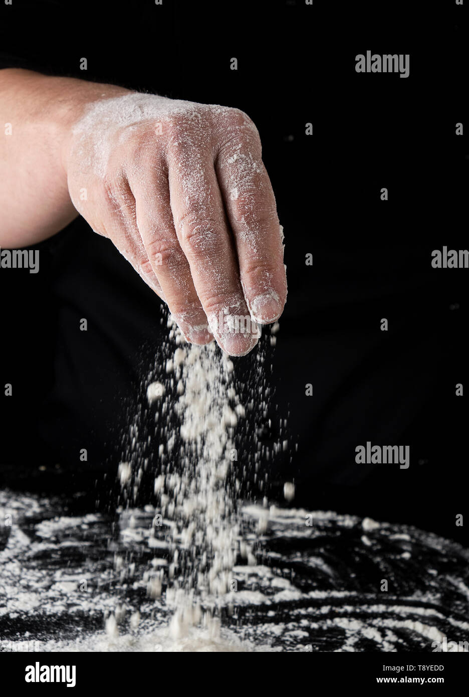 chef in black uniform sifts through his fingers white wheat flour over ...