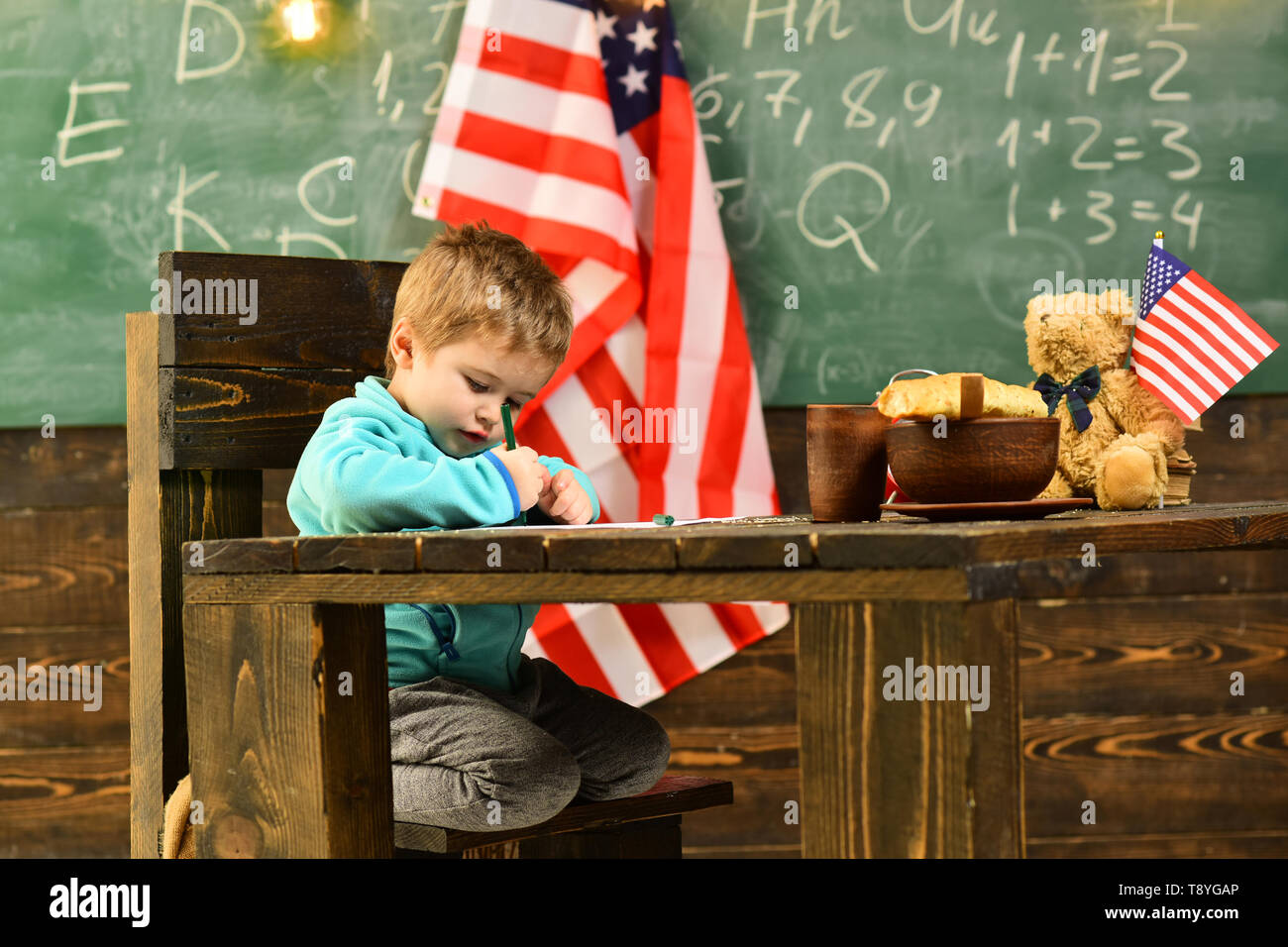 American preschool student drawing or writing near USA flag. Stock Photo
