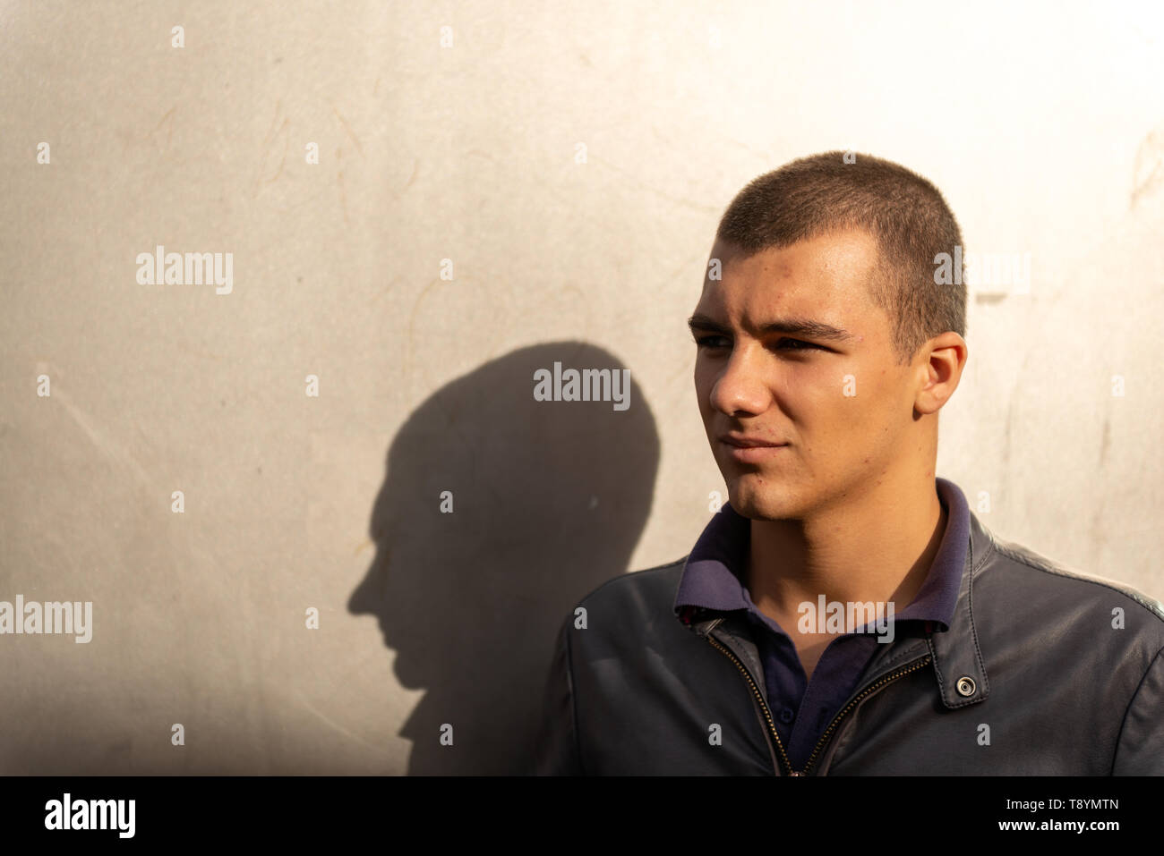 Portrait of 20-30 years young man and his shadow looking away and brightly lit background wall. MR Images of people with lots of copy space. Stock Photo