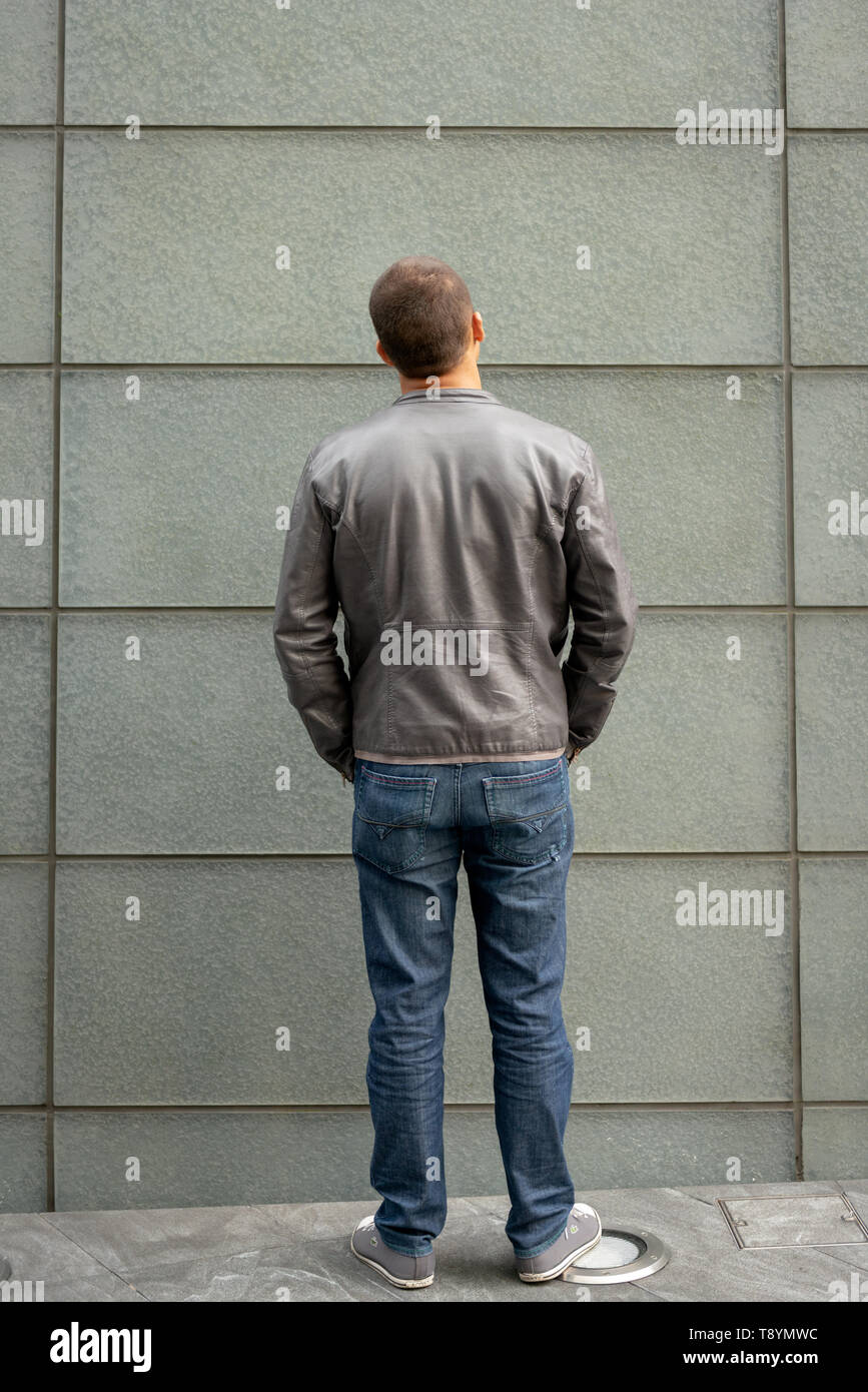Young 20-30 years man in full size with leather jacket and jeans standing still and looking into a wall. MR Images of people with lots of copy space. Stock Photo