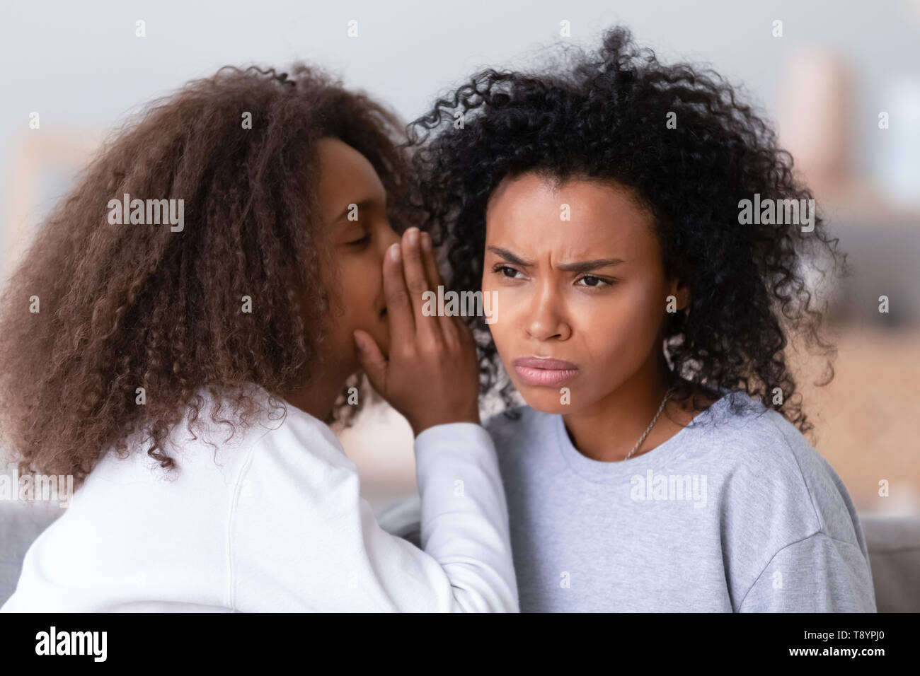 African American teen daughter whispering in unhappy mother ear Stock Photo