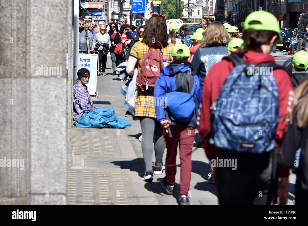 London, England, UK. Homeless man in the steet with a group of schoolchildren walking past - the Strand Stock Photo