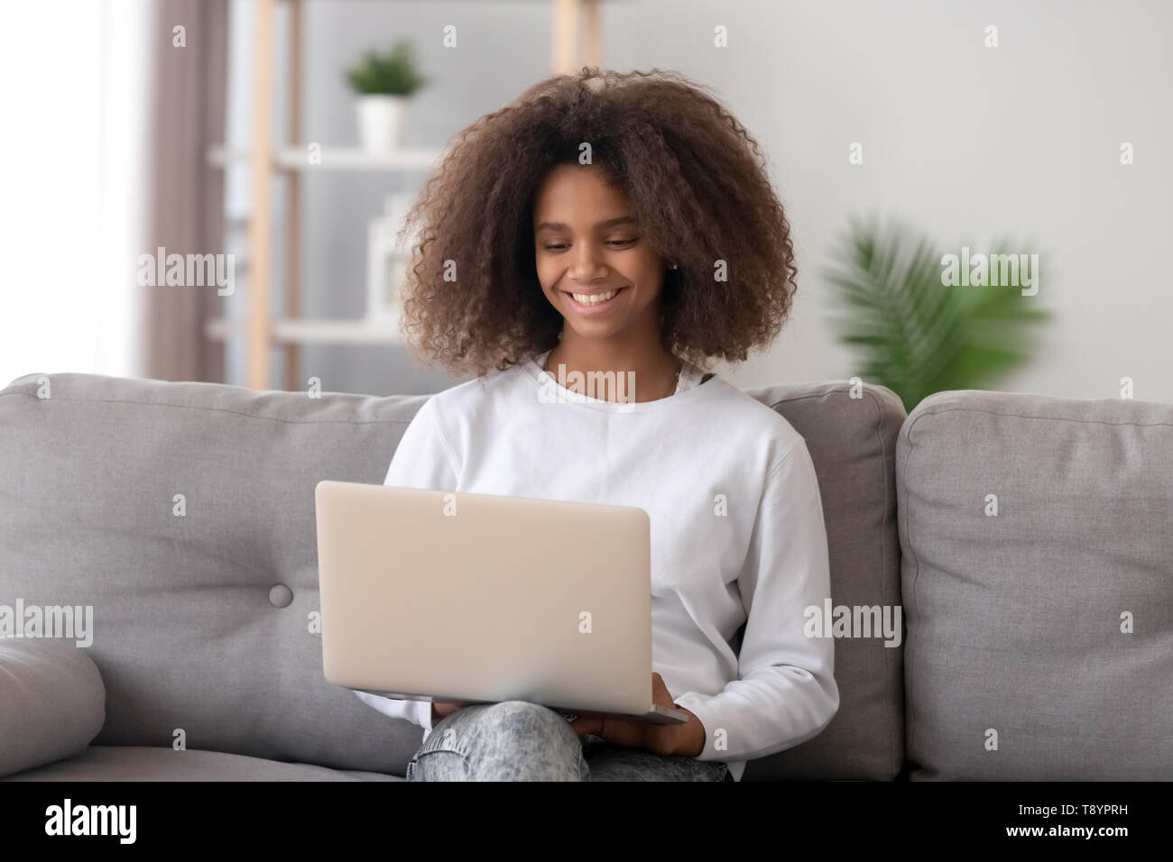Smiling African American teenage girl using laptop, looking at screen ...