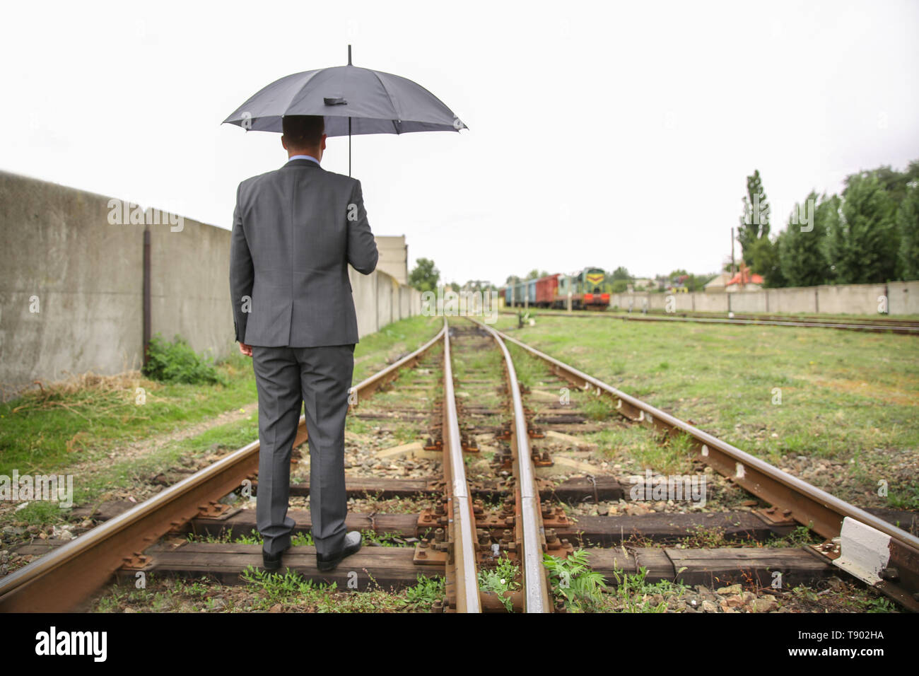 Businessman with umbrella standing railway track. Concept of choice