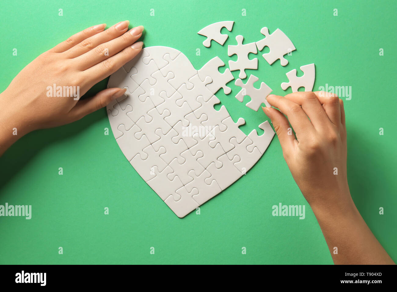 Woman doing jigsaw puzzle on color background Stock Photo