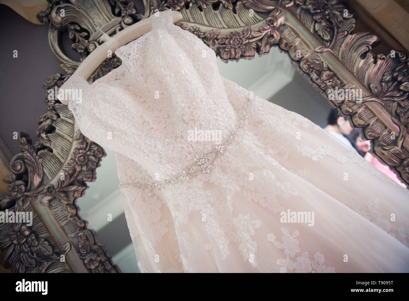Plus size wedding dress hanging from mirror Stock Photo