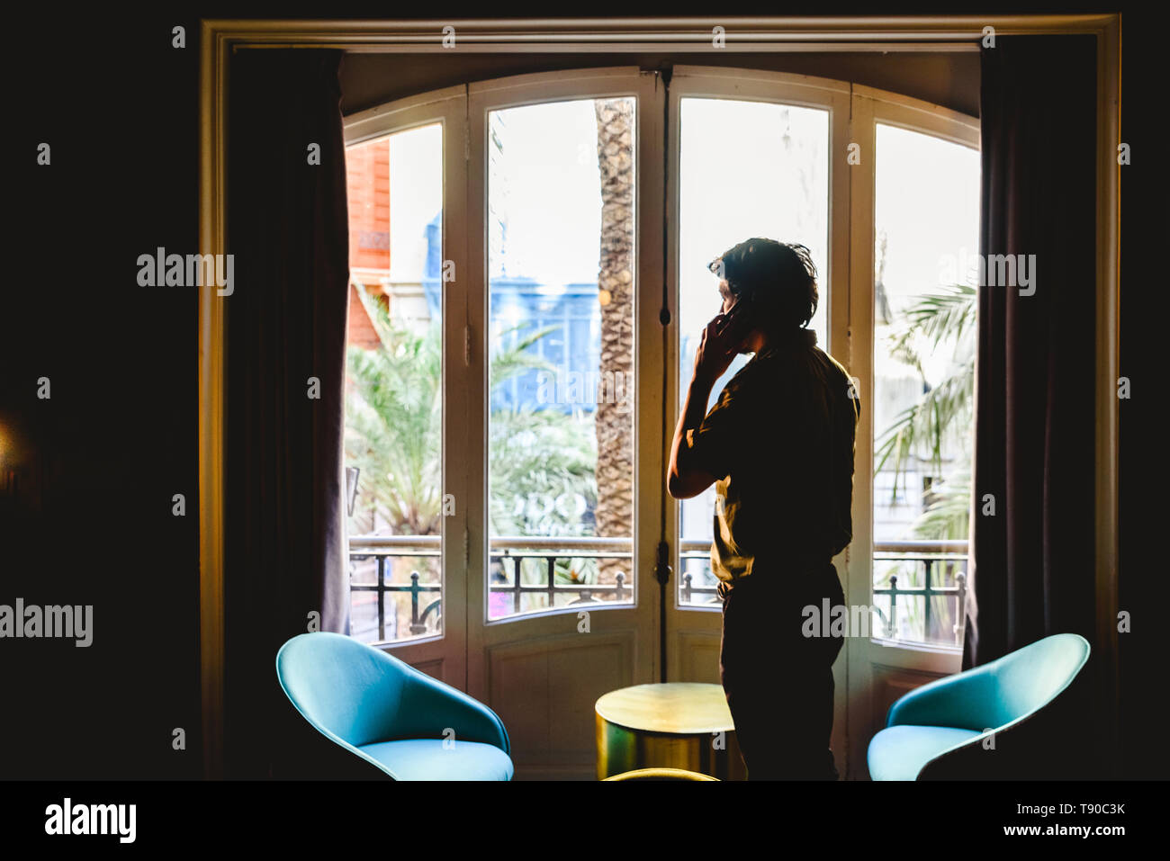 Entrepreneur man attending a phone call in his office in front of a large window. Stock Photo