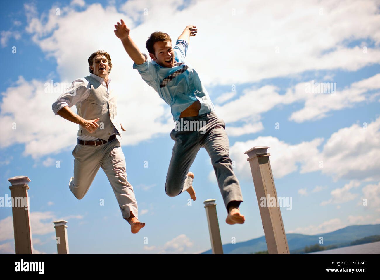 Two well dressed male friends jumping for joy on a jetty. Stock Photo