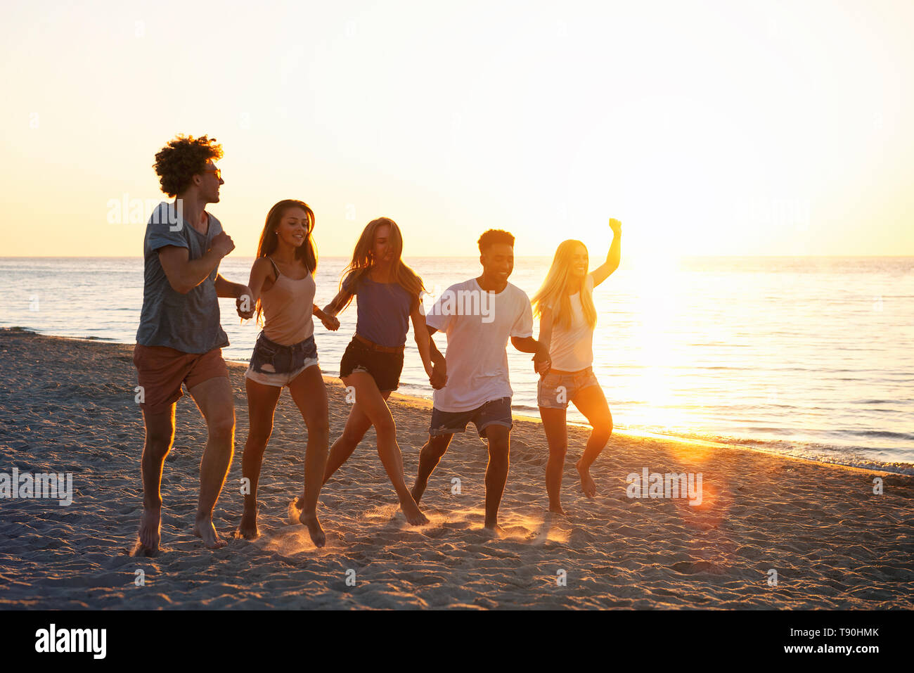 Group of happy friends having fun at ocean beach at dawn Stock Photo