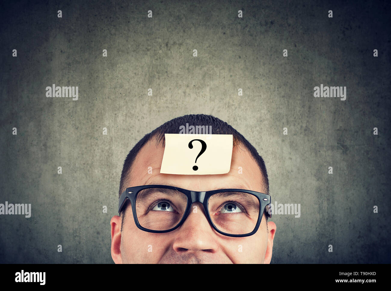thinking man in glasses with question mark looking up on gray wall background Stock Photo
