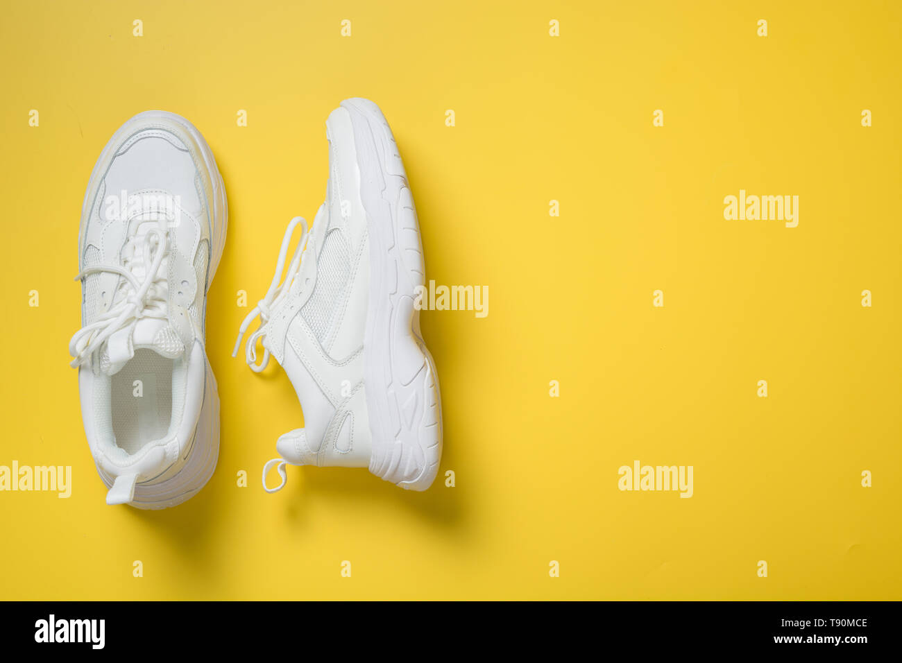 Pair of white female sneakers on yellow. Flat lay, top view minimal background. Magazine concept. Stock Photo