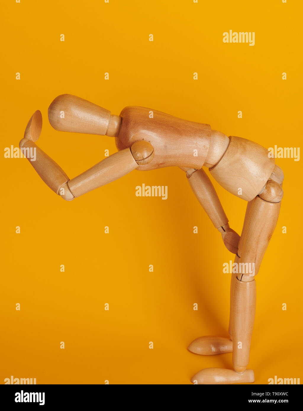 Wooden man in tired pose isolated on yellow background Stock Photo