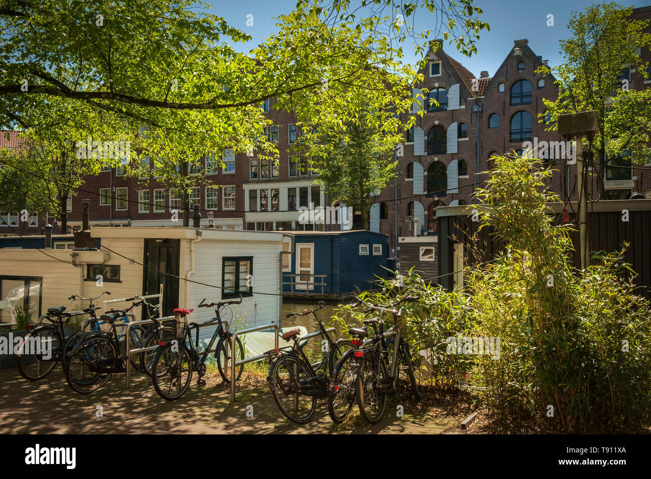 Houseboats, warehouses, cycle racks and greenery along an Amsterdam canal. Stock Photo