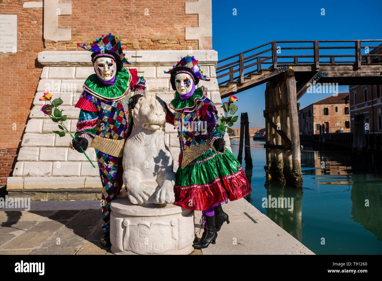 A masked couple in a beautiful creative costumes, posing at the buildings of Arsenale, celebrating the Venetian Carnival Stock Photo