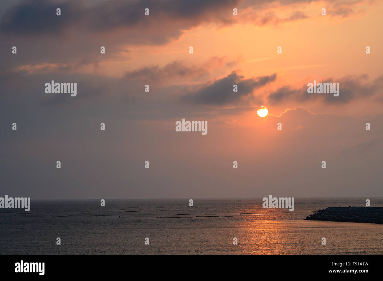 Seascape at Yellow glowing sun setting in the horizon with breakwater. Stock Photo