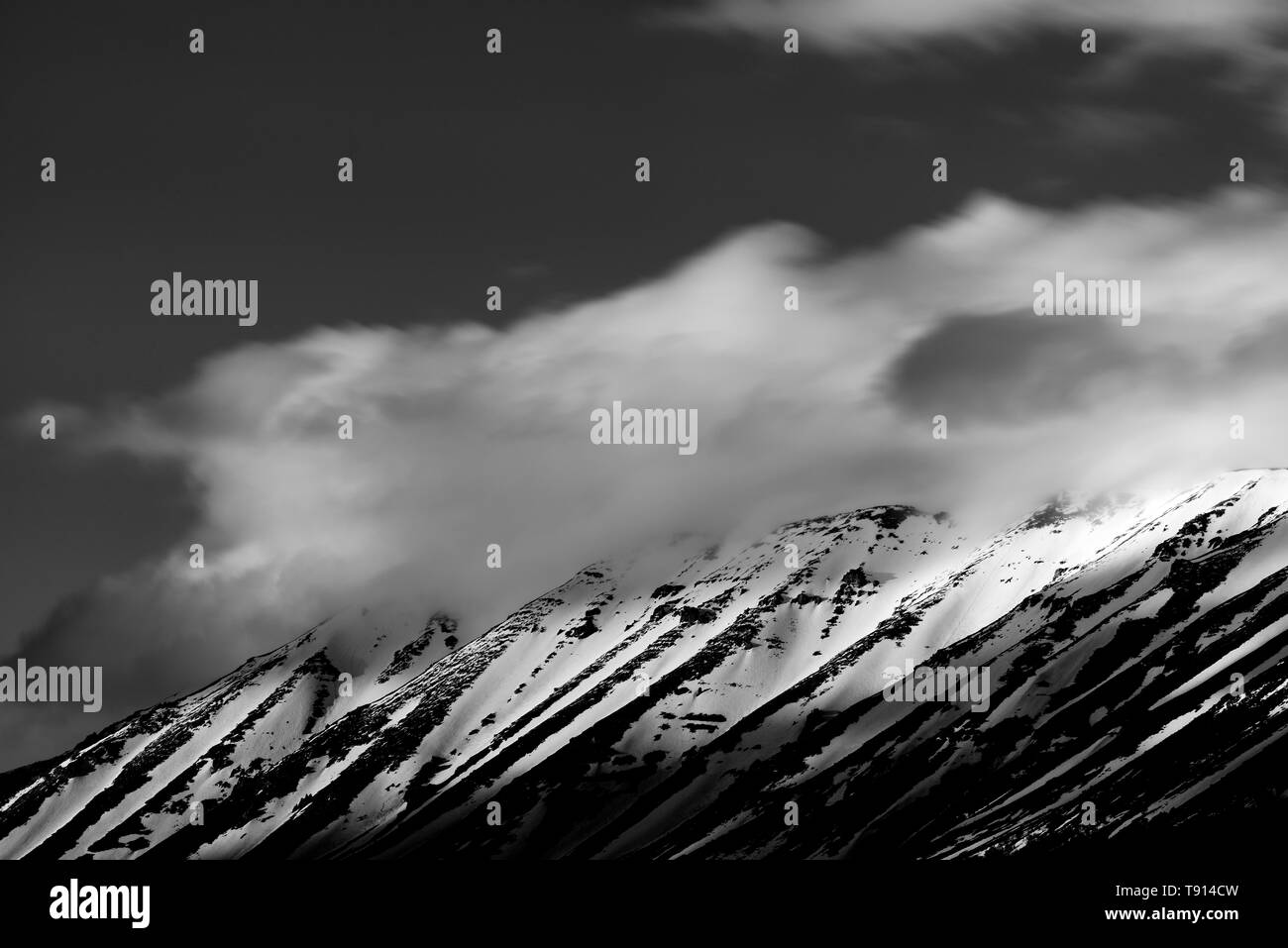 Clouds moving over the top of a mountain covered with snow and hit by the sun Stock Photo