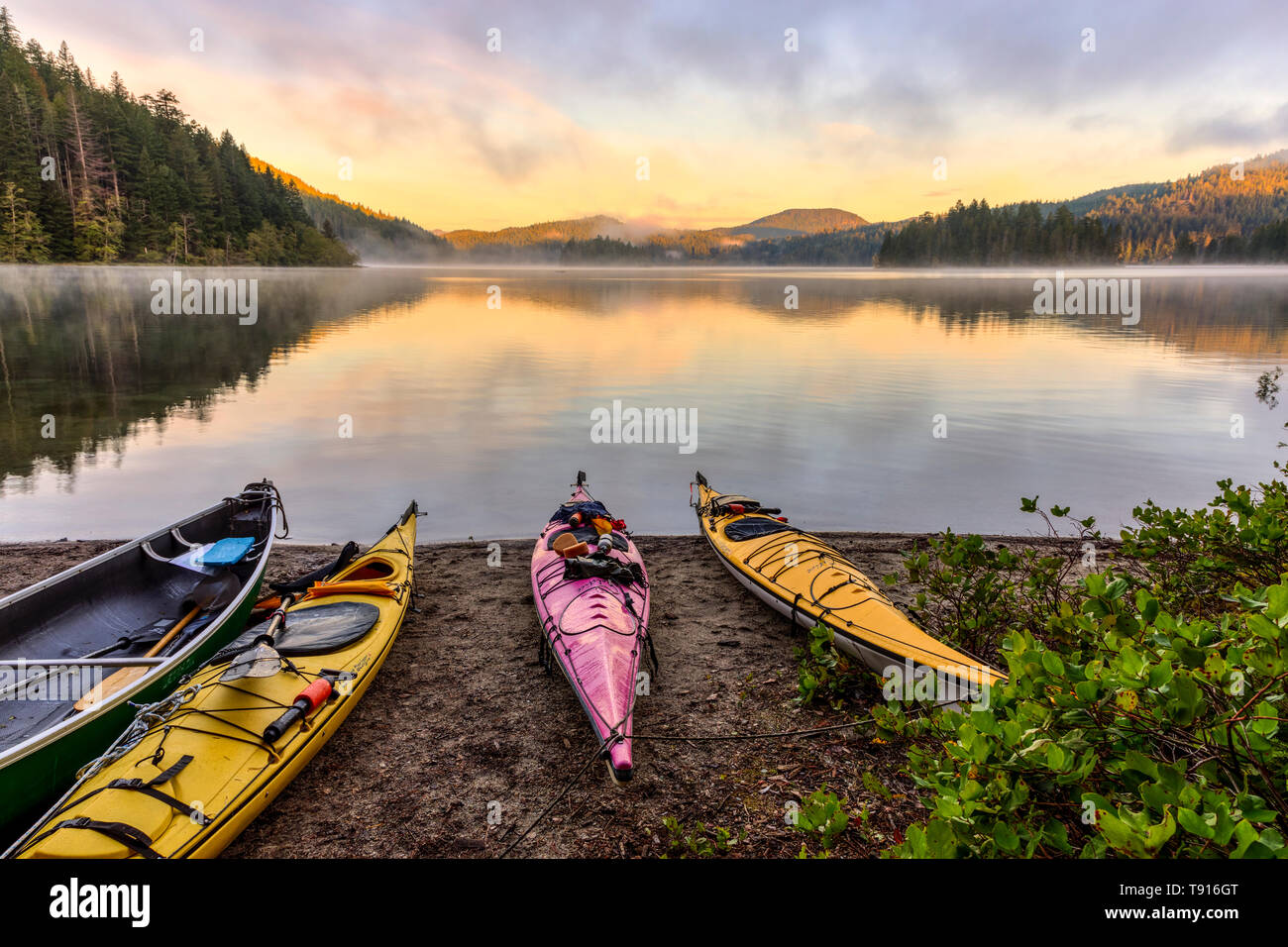 Kayaks and a canoe rest on the shore of Main Lake, in Main Lake Provincial Park on Quadra Island, British Columbia, Canada. Stock Photo