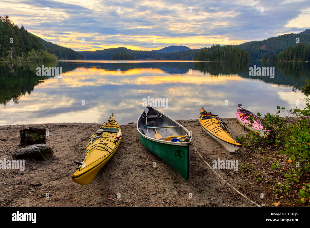 Kayaks and a canoe rest on the shore of Main Lake, in Main Lake Provincial Park on Quadra Island, British Columbia, Canada. Stock Photo
