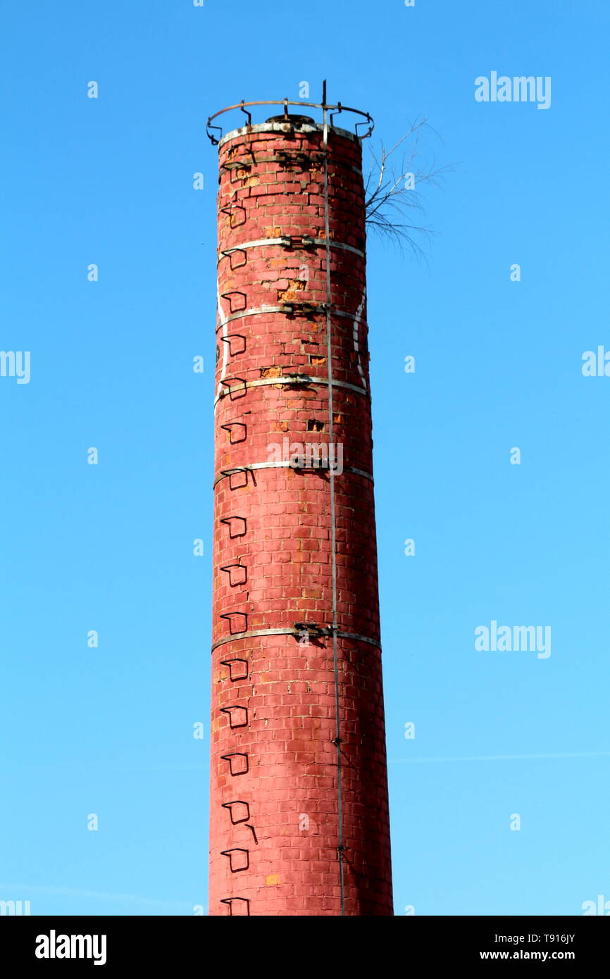 Tall red brick industrial chimney with metal lightning rod and steps