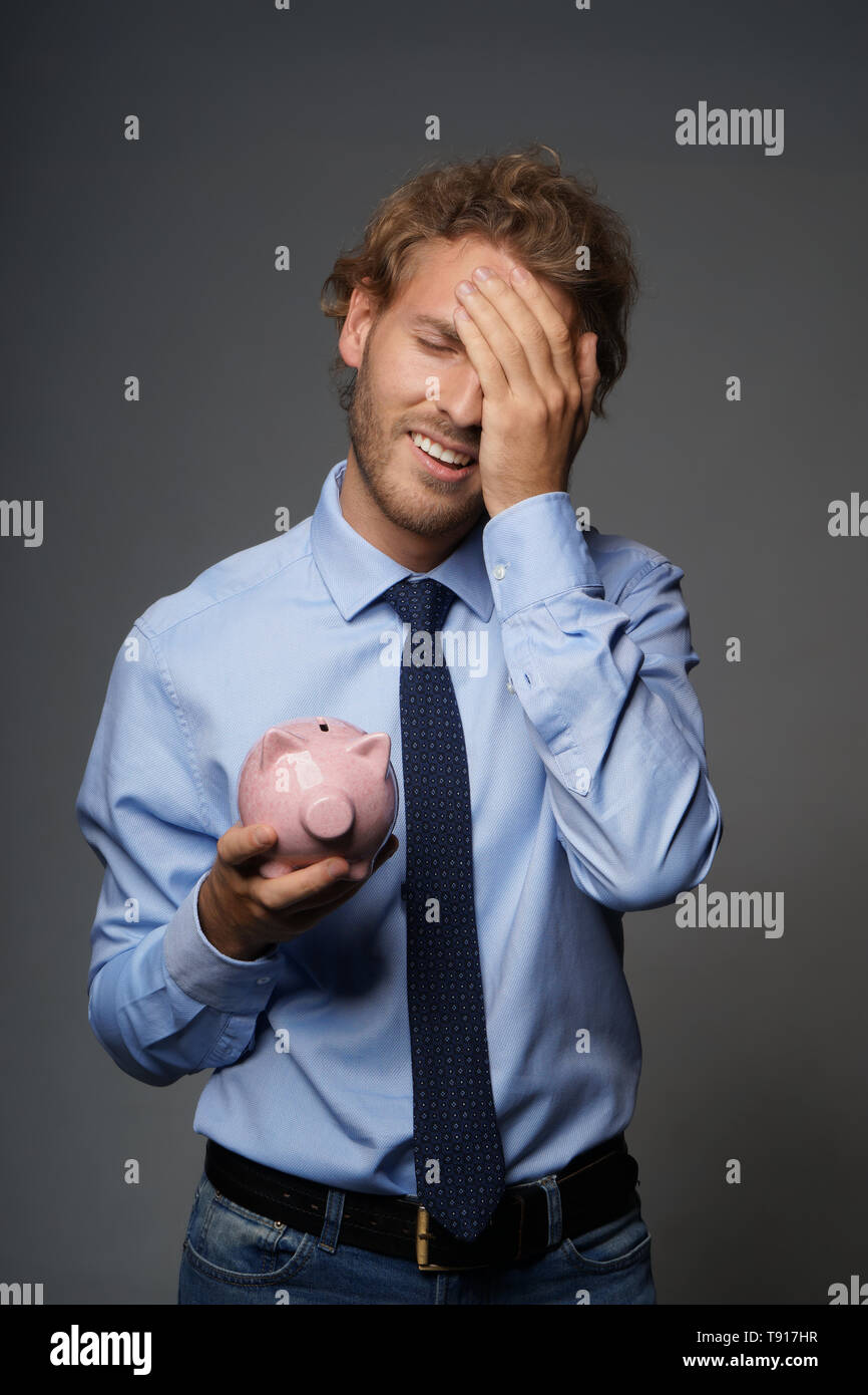 Upset man with piggy bank on grey background Stock Photo - Alamy