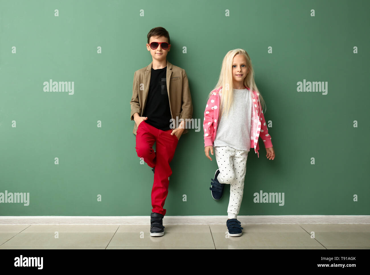 Cute boy and girl in fashionable clothes near color wall Stock