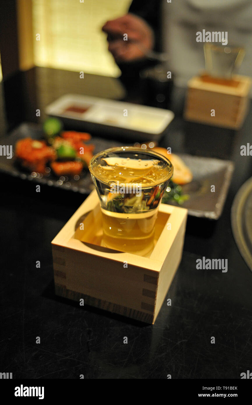 Full sake cup in a wooden box on a table in a restaurant in Tokyo Stock Photo