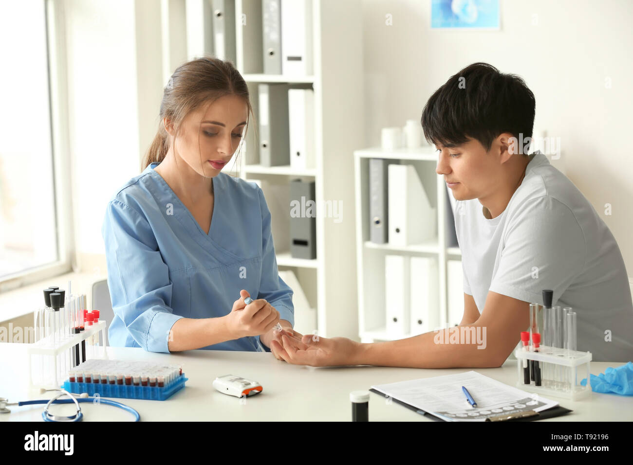 Doctor taking patient's blood sample with lancet pen in hospital Stock