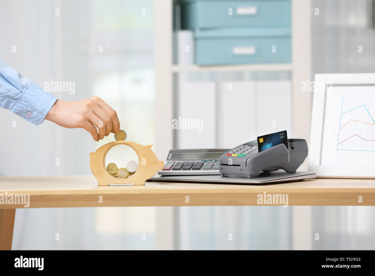 Woman putting coin into piggy bank on wooden table Stock Photo - Alamy