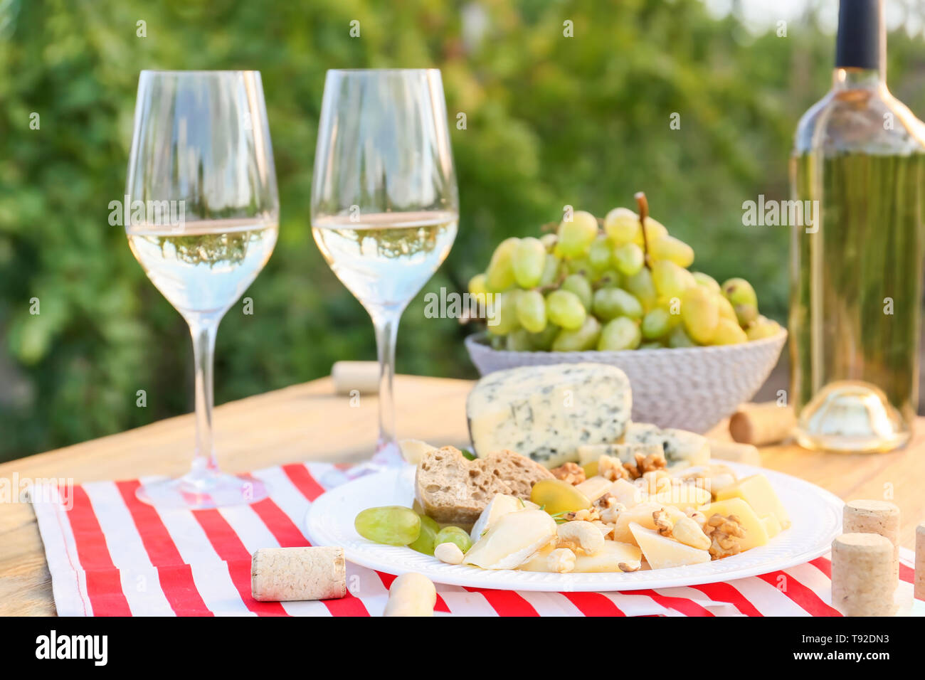 Glasses and bottle of white wine with snacks on table in vineyard Stock