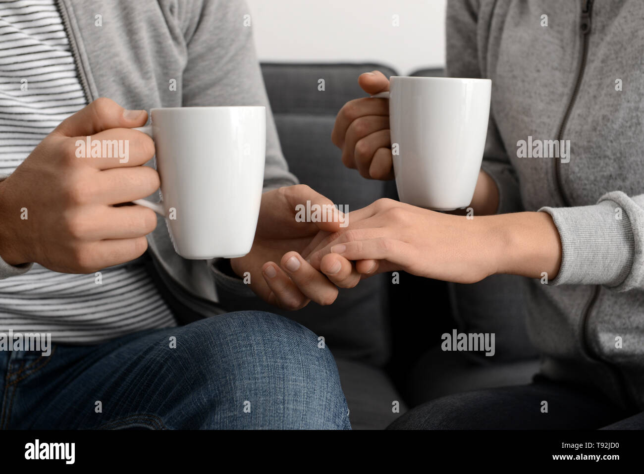 Young couple with cups of tea holding hands at home Stock Photo - Alamy