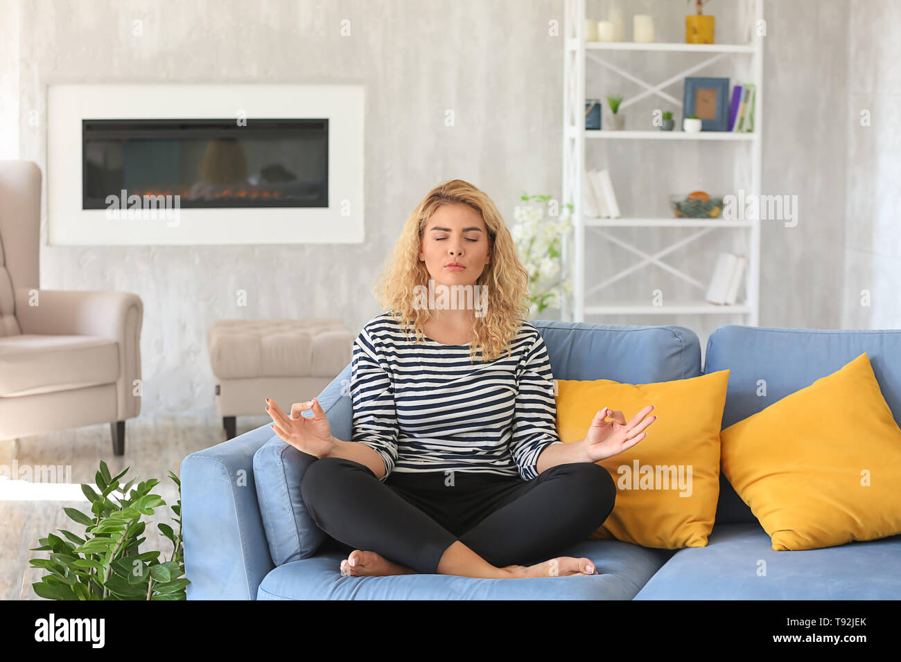 Beautiful young woman meditating at home Stock Photo - Alamy