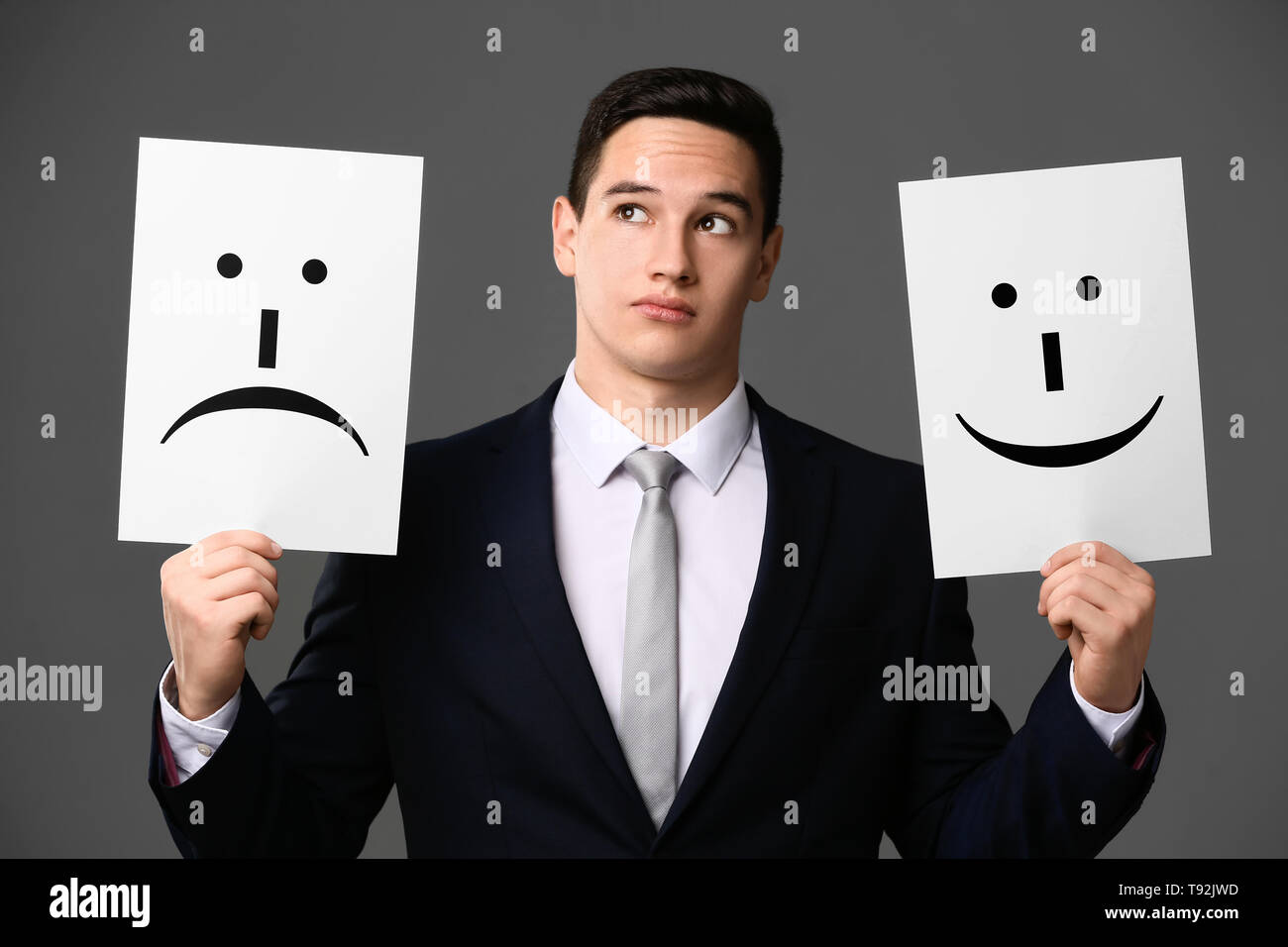 Businessman holding sheets of paper with drawn emoticons on grey background Stock Photo