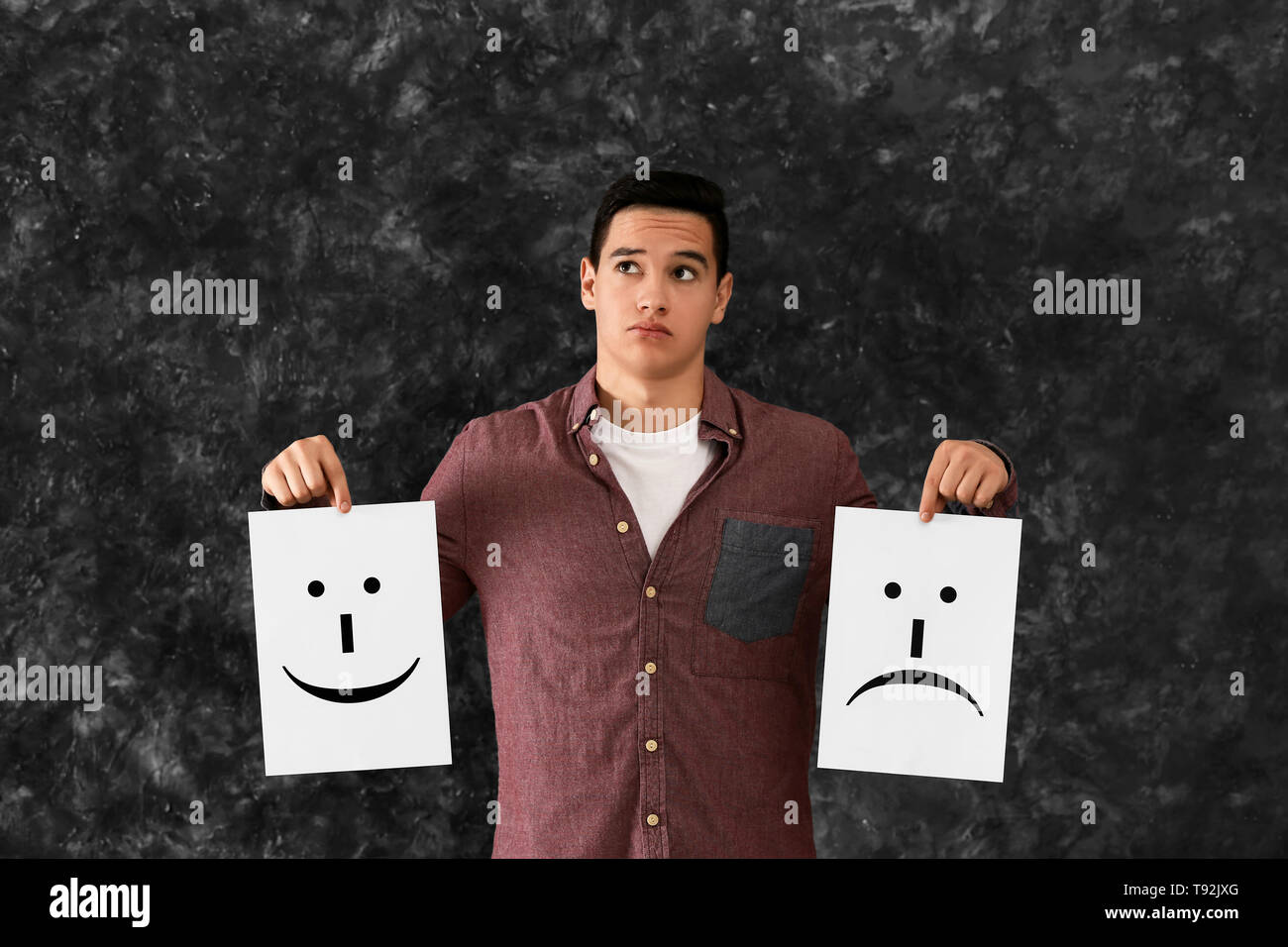 Young man holding sheets of paper with drawn emoticons on grey background Stock Photo