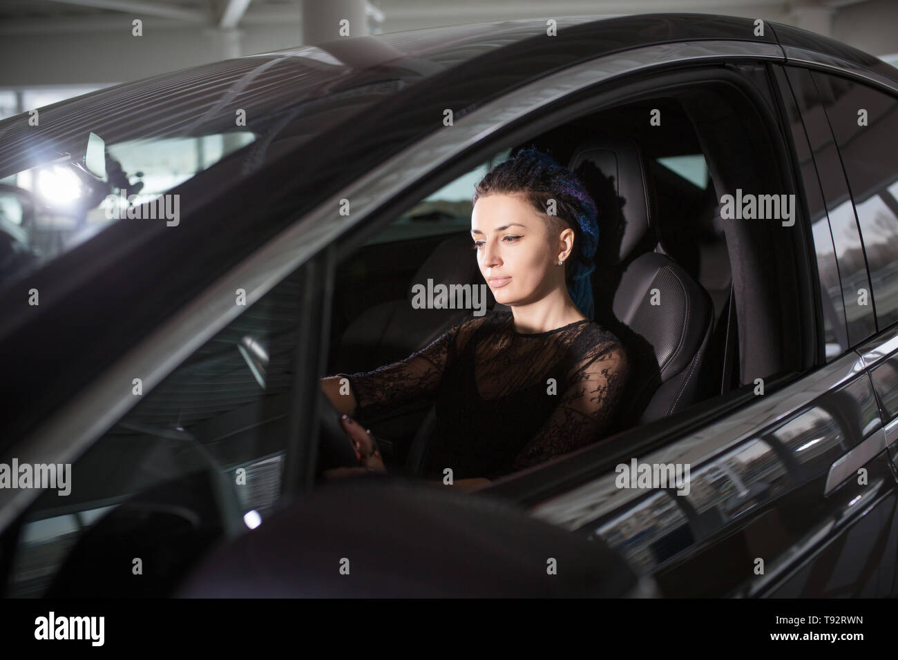 Girl is Driving Expensive Tesla Electromobile in Auto Show. Stock Photo