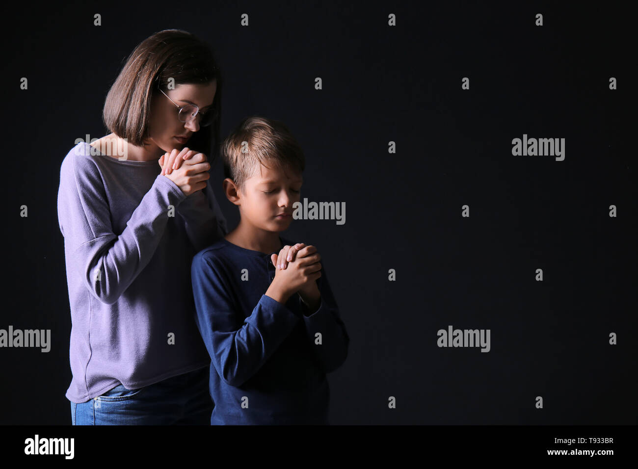 Praying mother and son on dark background Stock Photo - Alamy