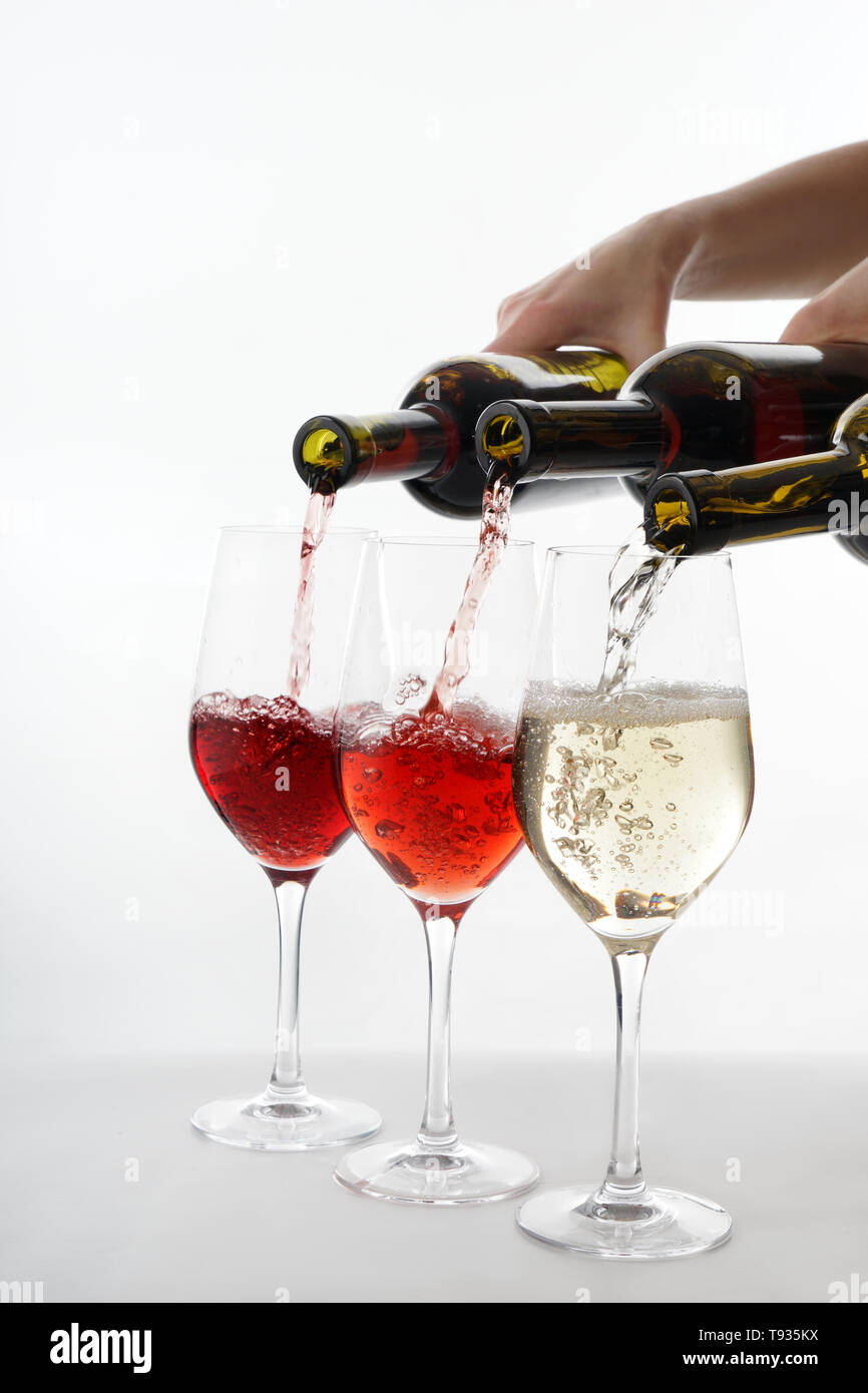 Pouring of different wine from bottles into glasses on white background