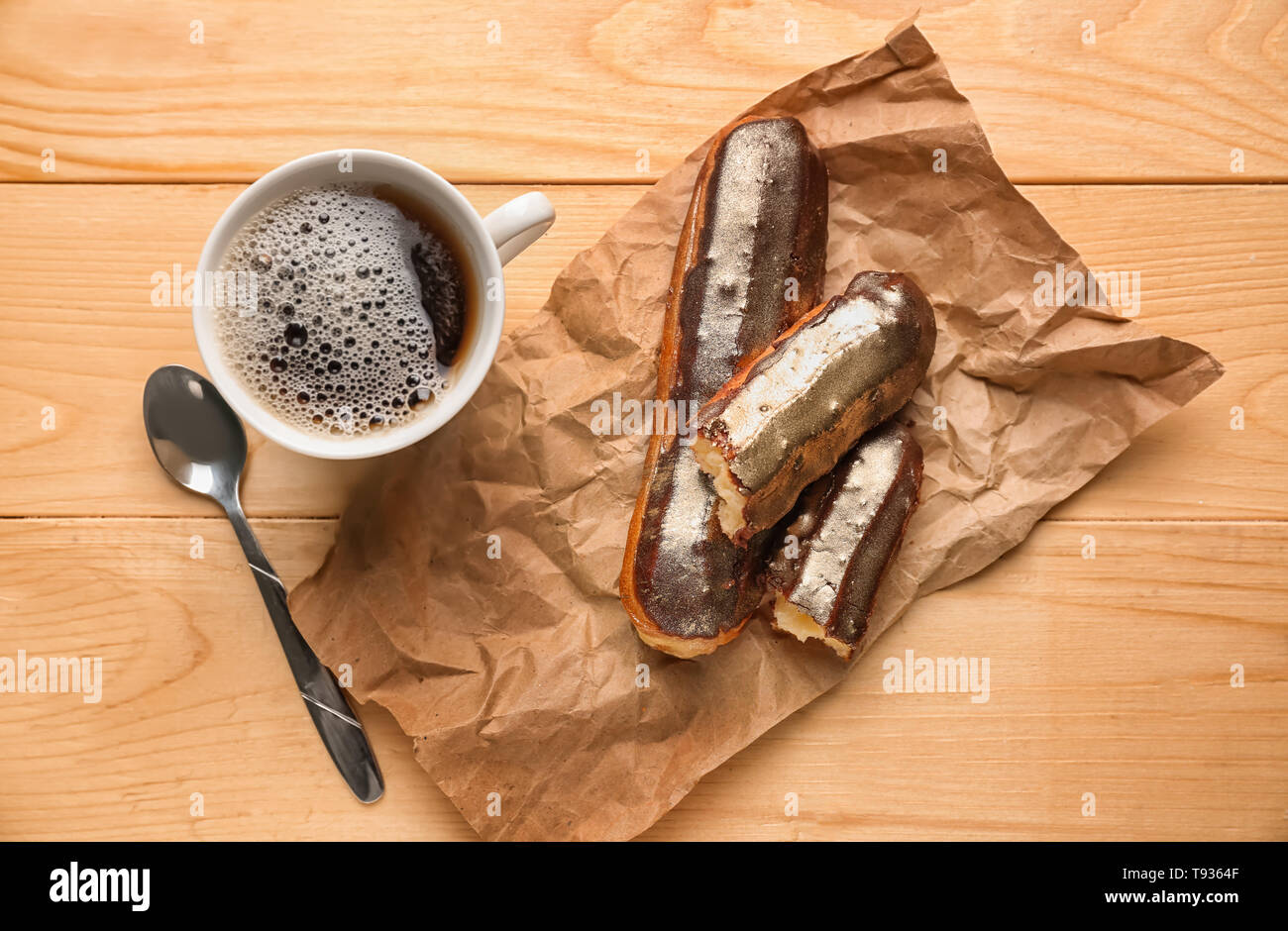 Delicious eclairs and cup of coffee on wooden table, top view Stock Photo