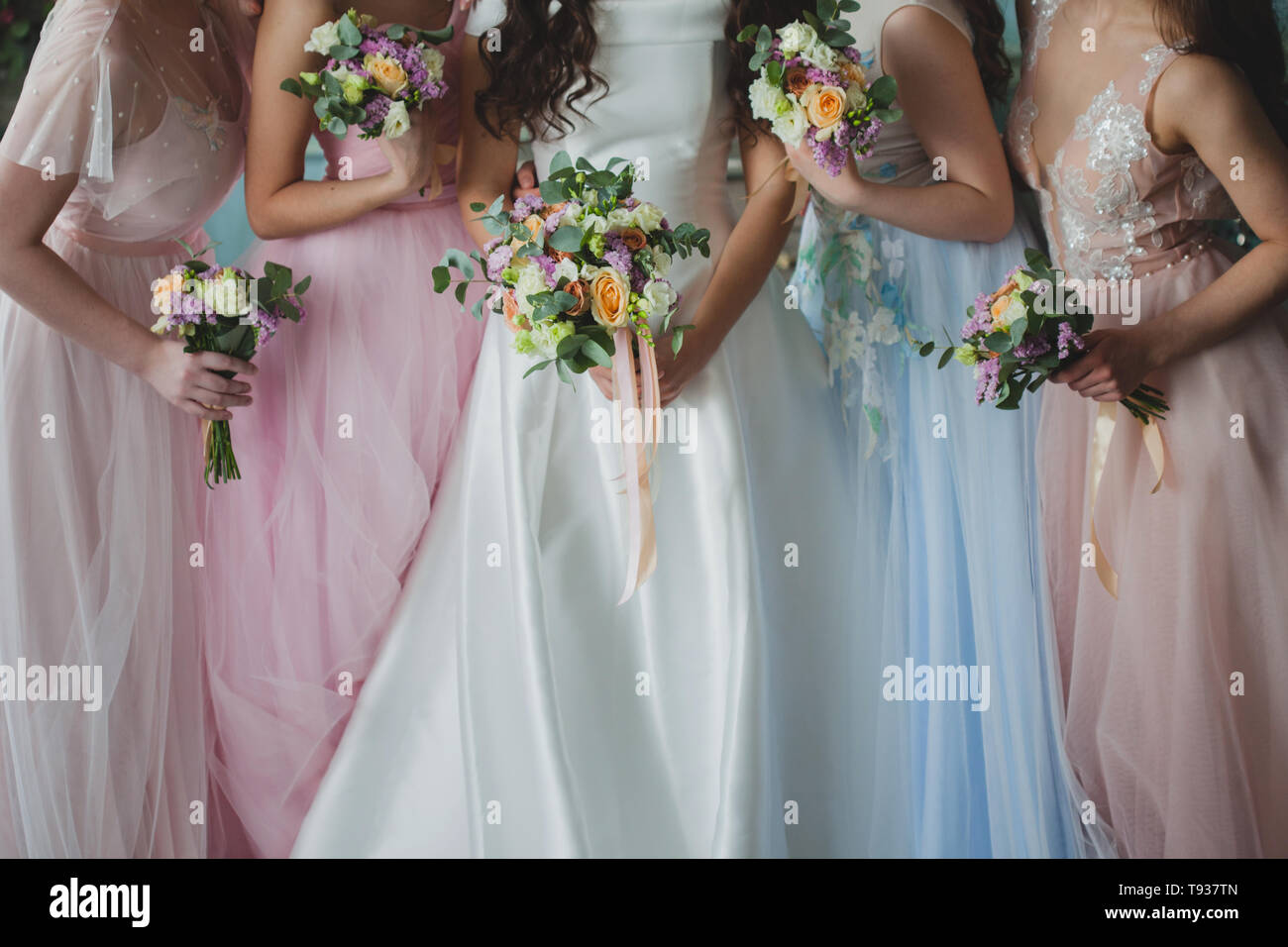 Bride and bridesmaids. Beautiful young women in dresses and with bouquets of fresh flowers. Stock Photo