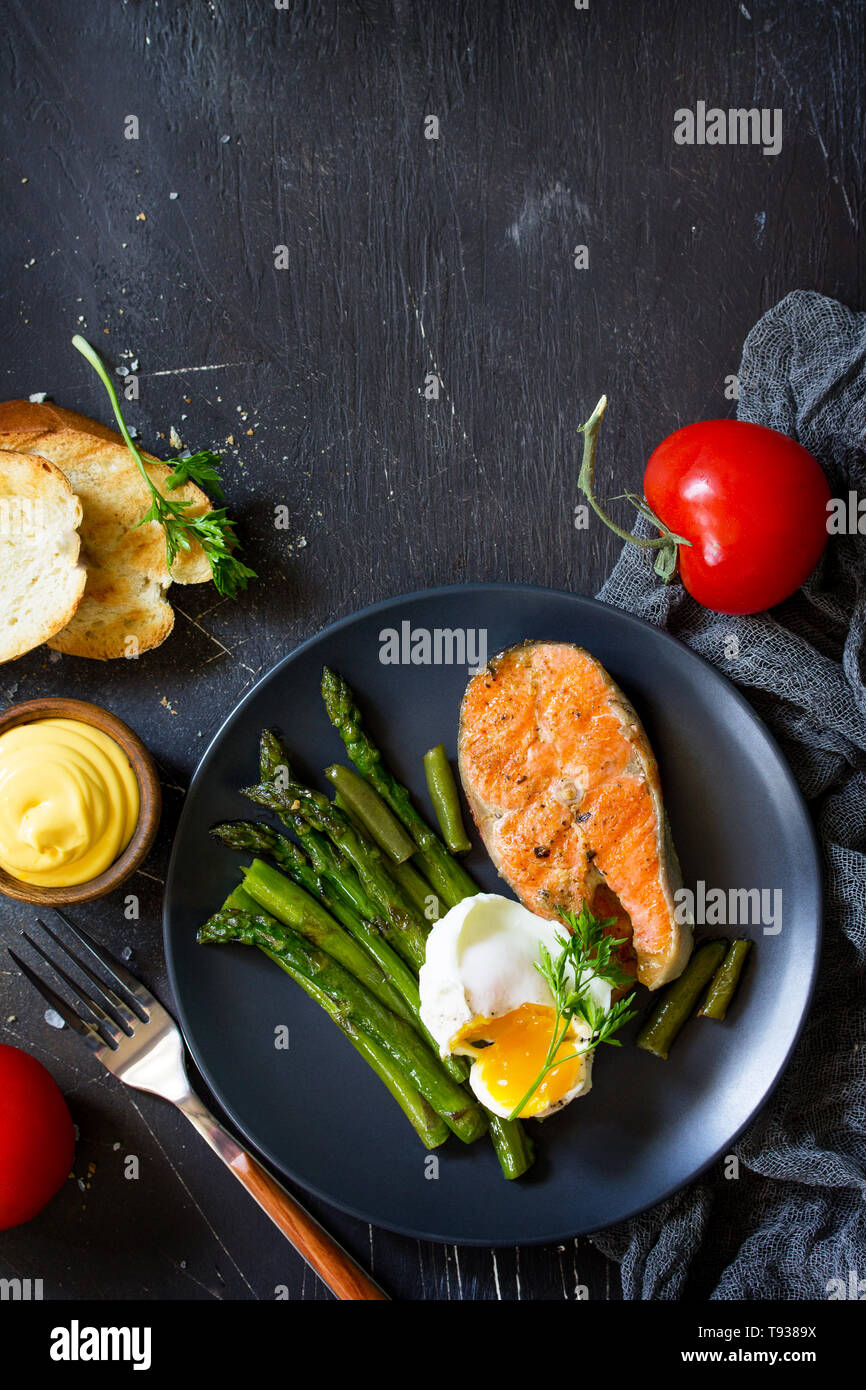 Salmon fish steak grilled with asparagus, poached egg on black background. Healthy food. Top view flat lay.  Free space for your text. Stock Photo