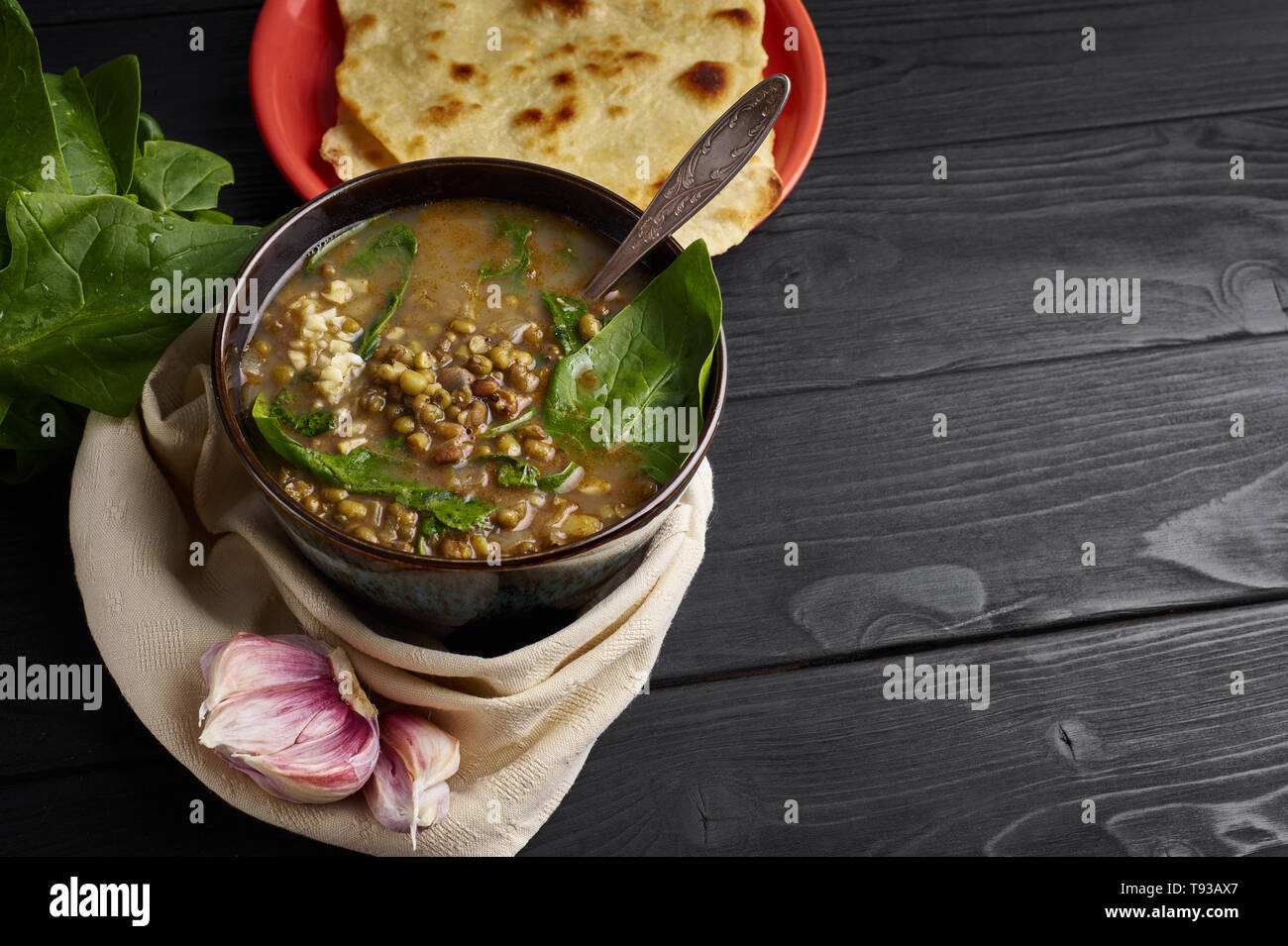 Mung Dhal with Spinach, Chapati and garlic at black wooden tabletop
