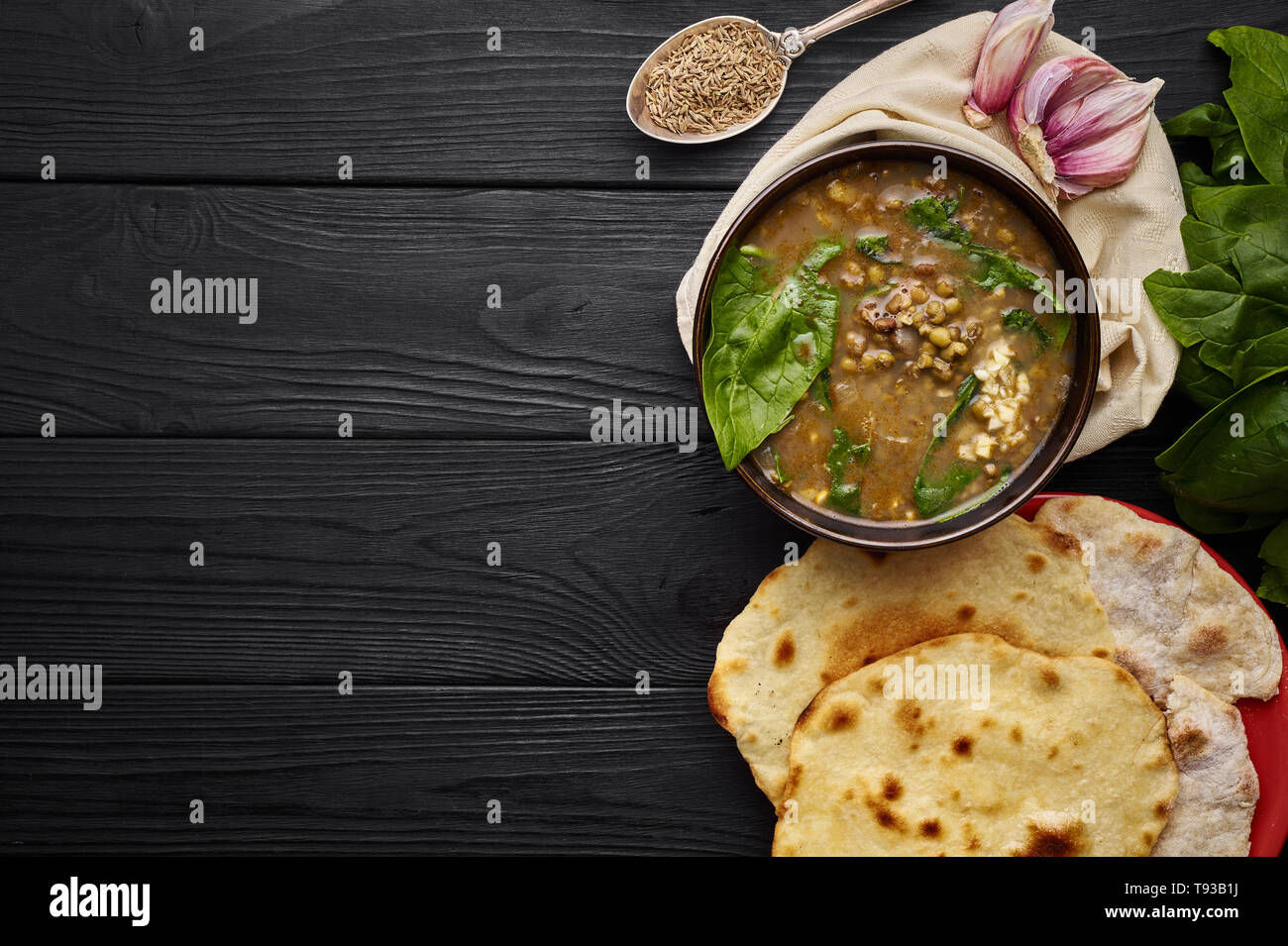 Mung Dhal, Spinach, Chapati, garlic and spices at black wooden tabletop