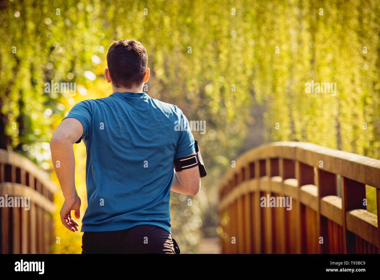 Rear view Male runner running in a city park over bridge training for ...