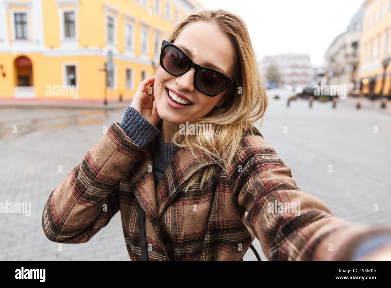 Beautiful young blonde woman wearing a coat taking a selfie while ...